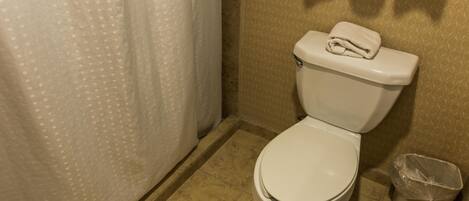 Un baño con inodoro, cortina de ducha y cubo de basura.