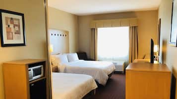Ein Hotelzimmer mit zwei Betten, einem Schreibtisch, einem Fernseher und einem Fenster mit Vorhängen.