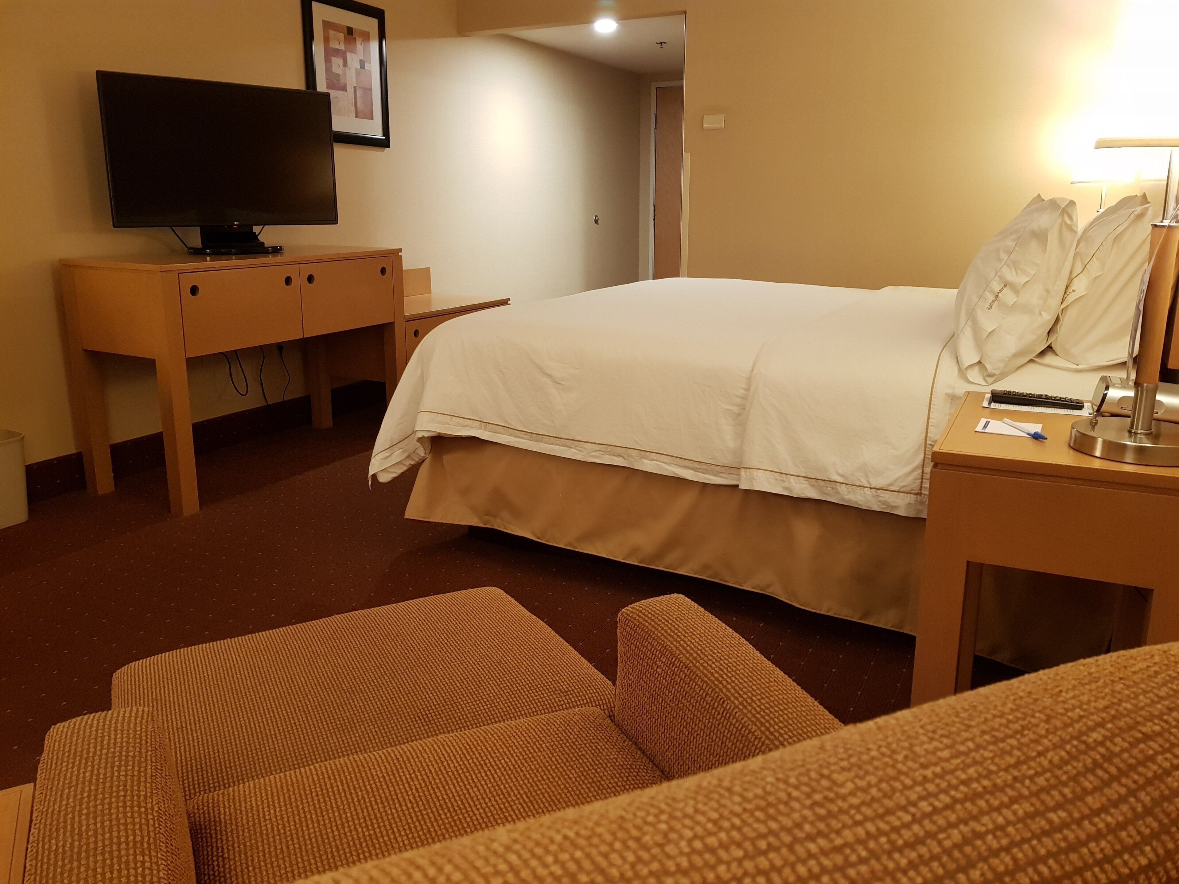 A hotel room with a bed, a television on a wooden cabinet, a desk with a lamp, and a chair.