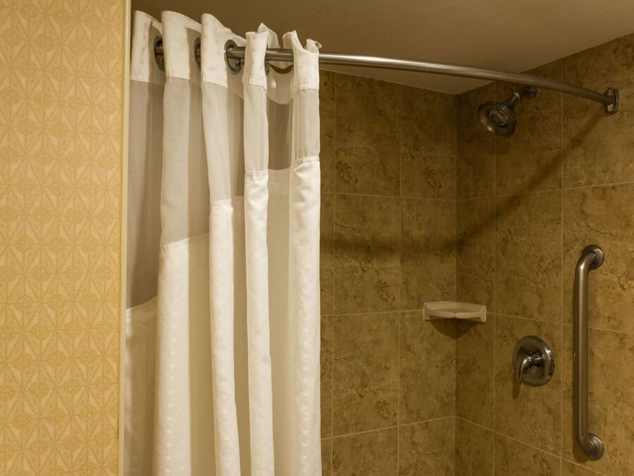 A shower area with a beige patterned wall, a white shower curtain, and a grab bar.