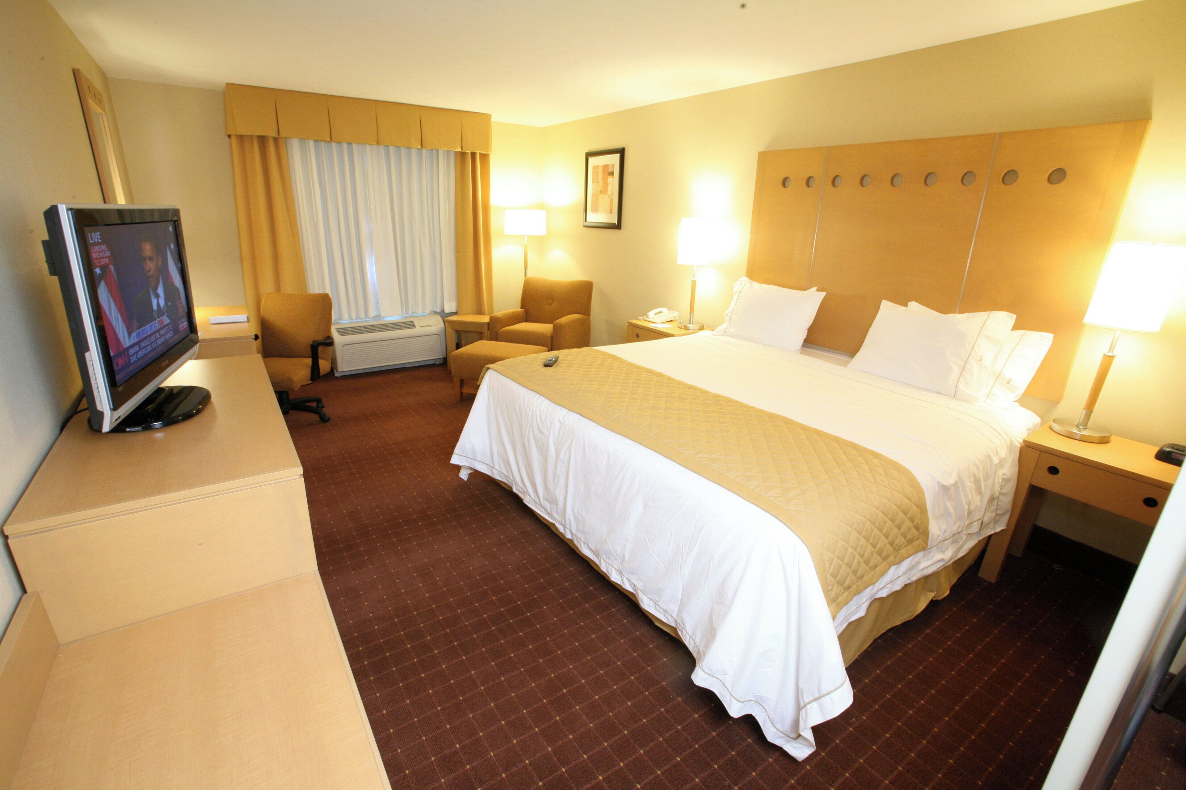 Une chambre d’hôtel avec un grand lit, des lampes de chevet, un bureau avec une télévision, une chaise et un appareil de climatisation.