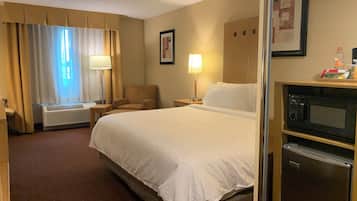 Habitació d'hotel amb un llit, una cadira, un escriptori, una làmpada, un quadre a la paret i un microones.