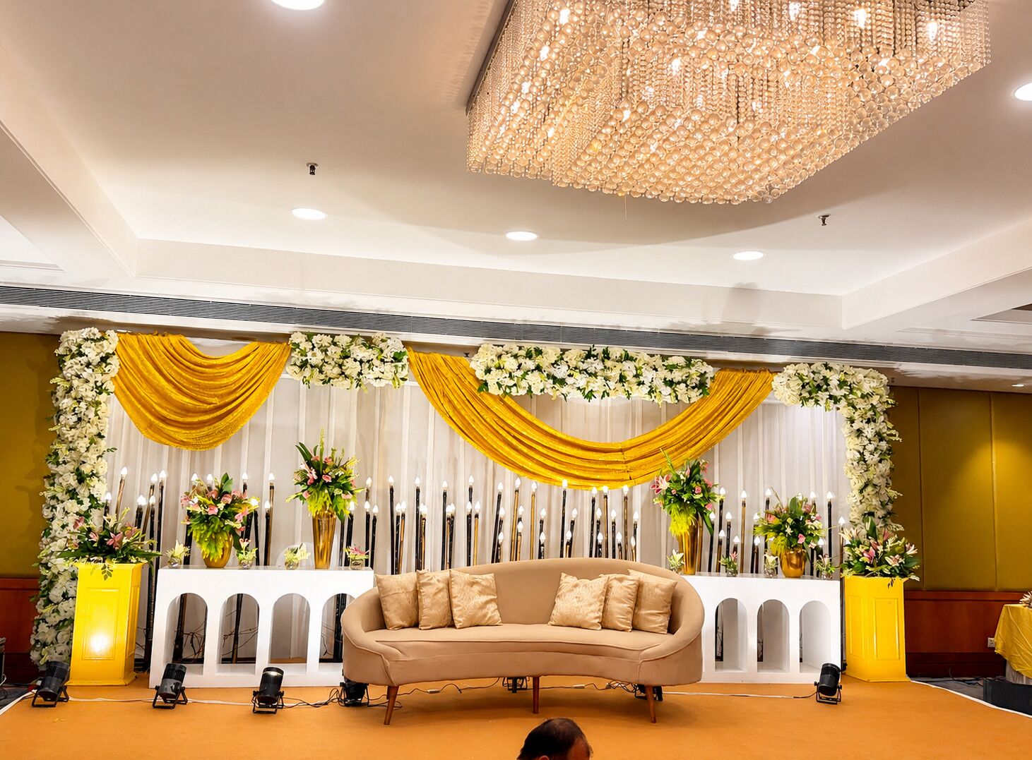 Um palco com um sofá, cortinas drapeadas e arranjos florais.