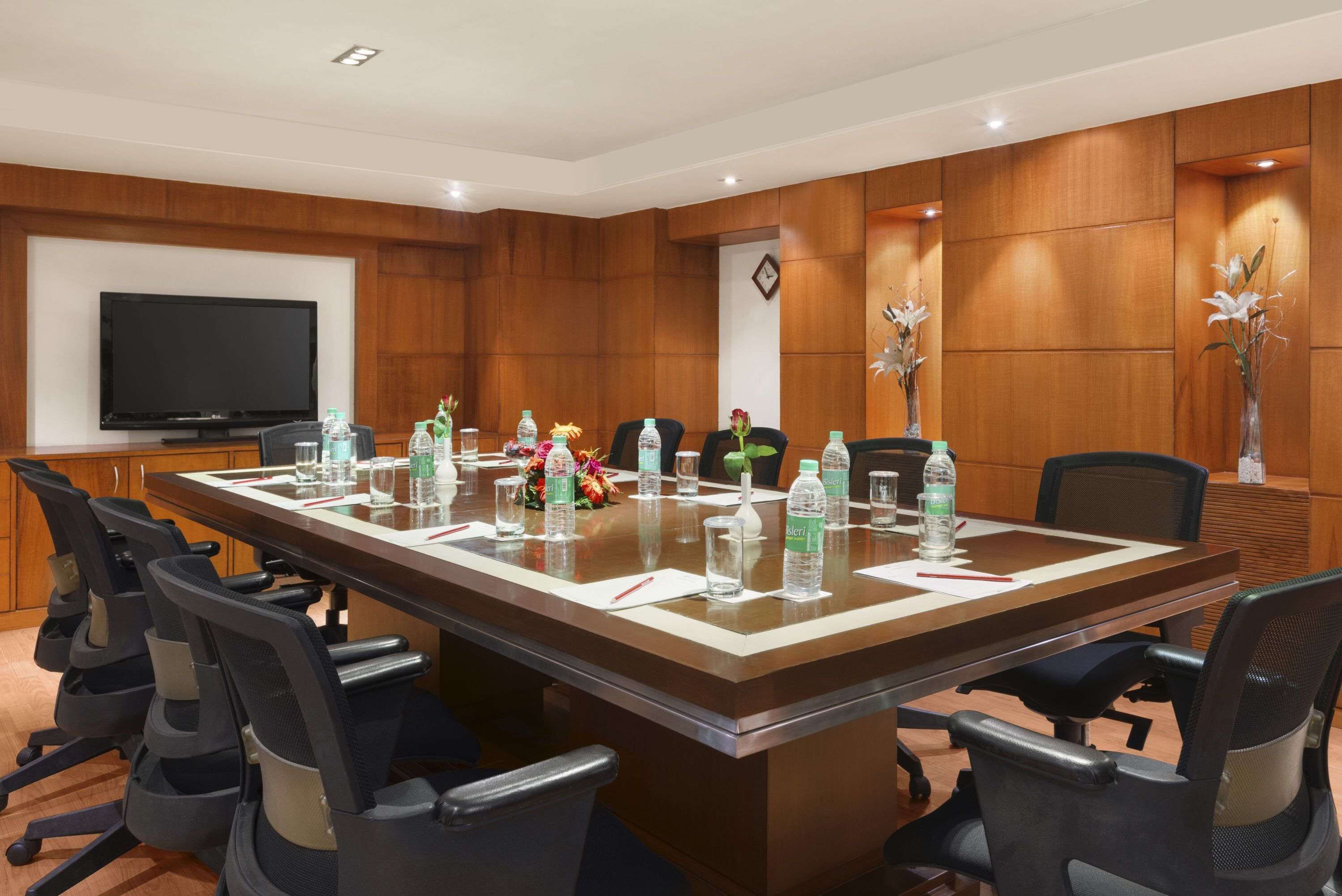 A conference room with a long table, chairs, a television, and decorative vases.