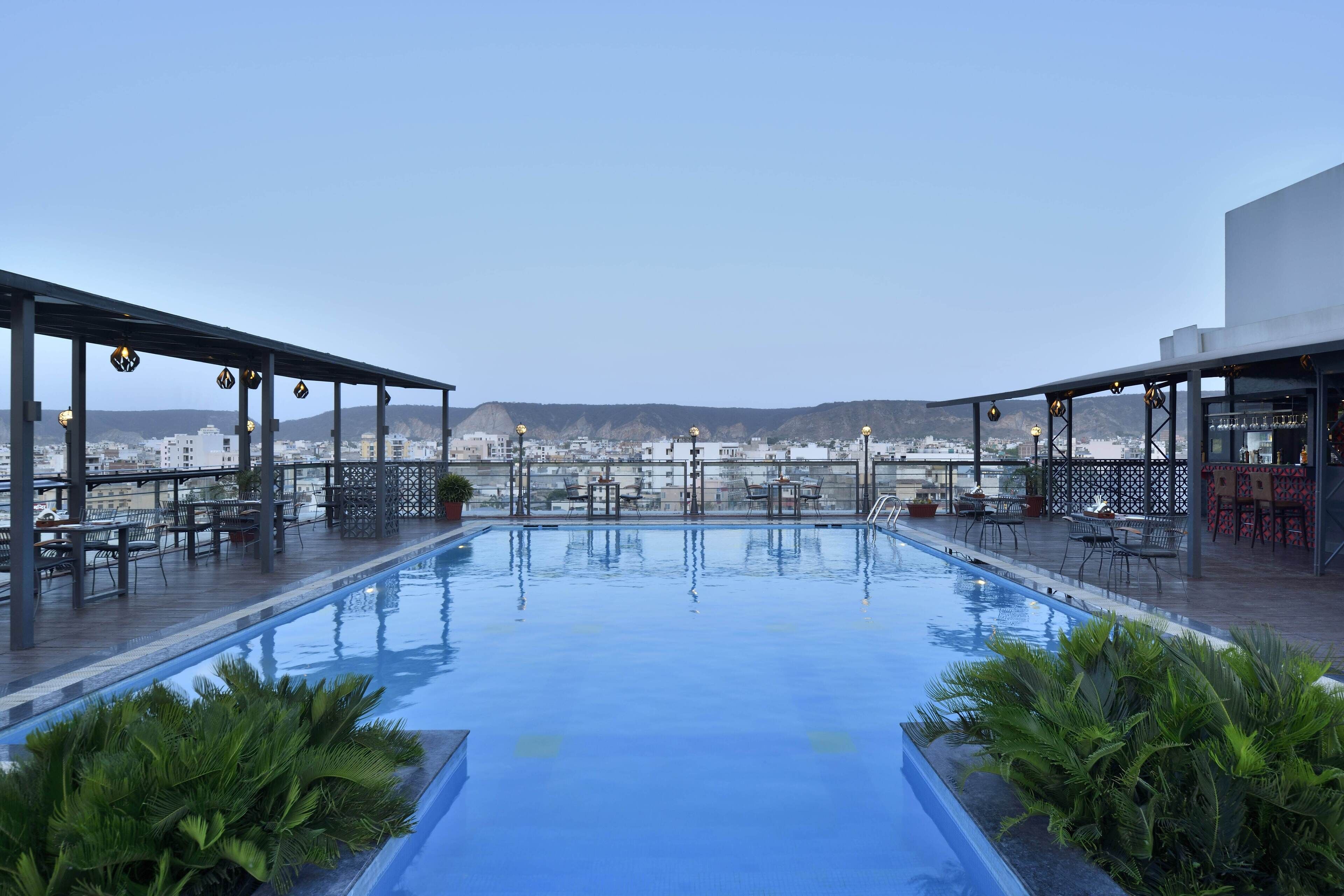 A rooftop pool with a clear view of the cityscape, surrounded by outdoor seating and greenery.