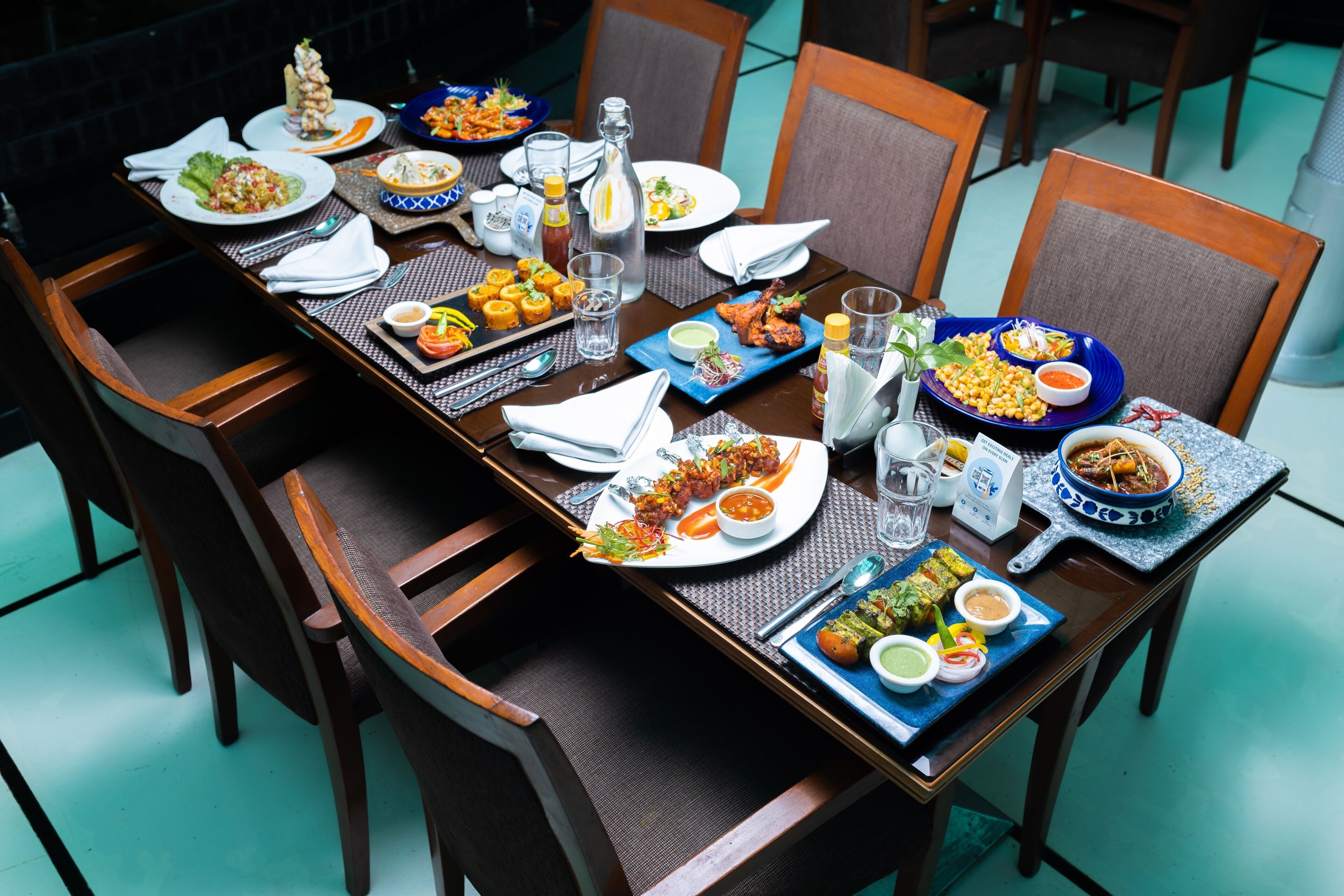 A dining table set with various dishes, glasses, and condiments, surrounded by wooden chairs.