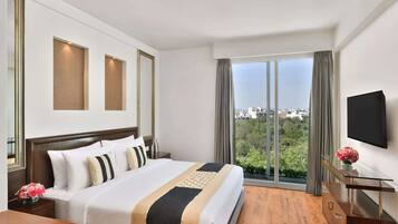 Quarto de hotel com uma cama grande, televisão na parede e janela com vista para a cidade.