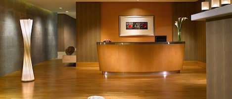 A reception area with a wooden reception desk, a framed artwork above it, and a vase with flowers on the right.