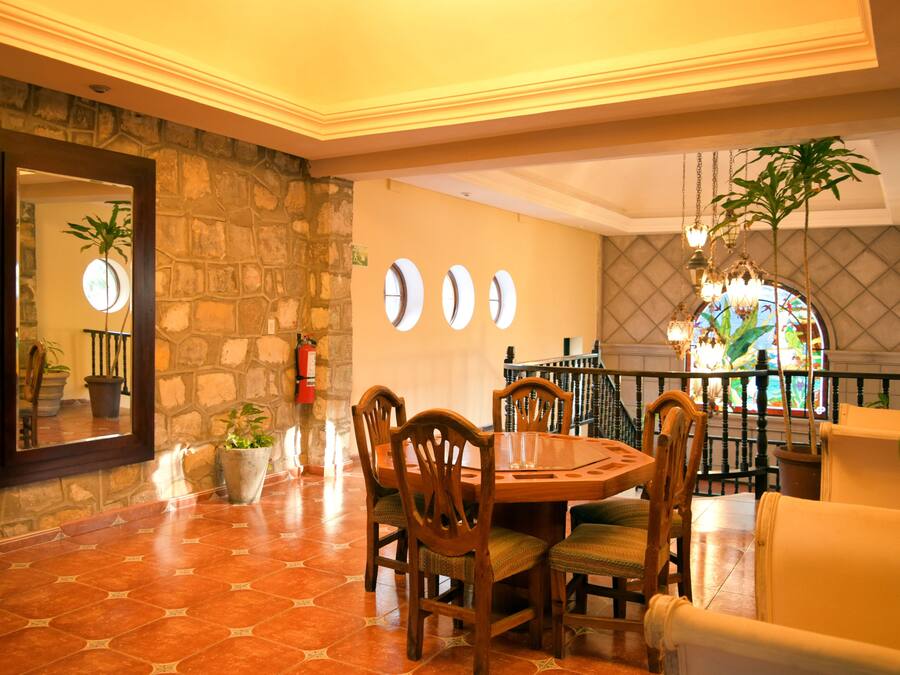 A dining area with a stone wall, a wooden table, and chairs. There are potted plants and a fire extinguisher on the wall.