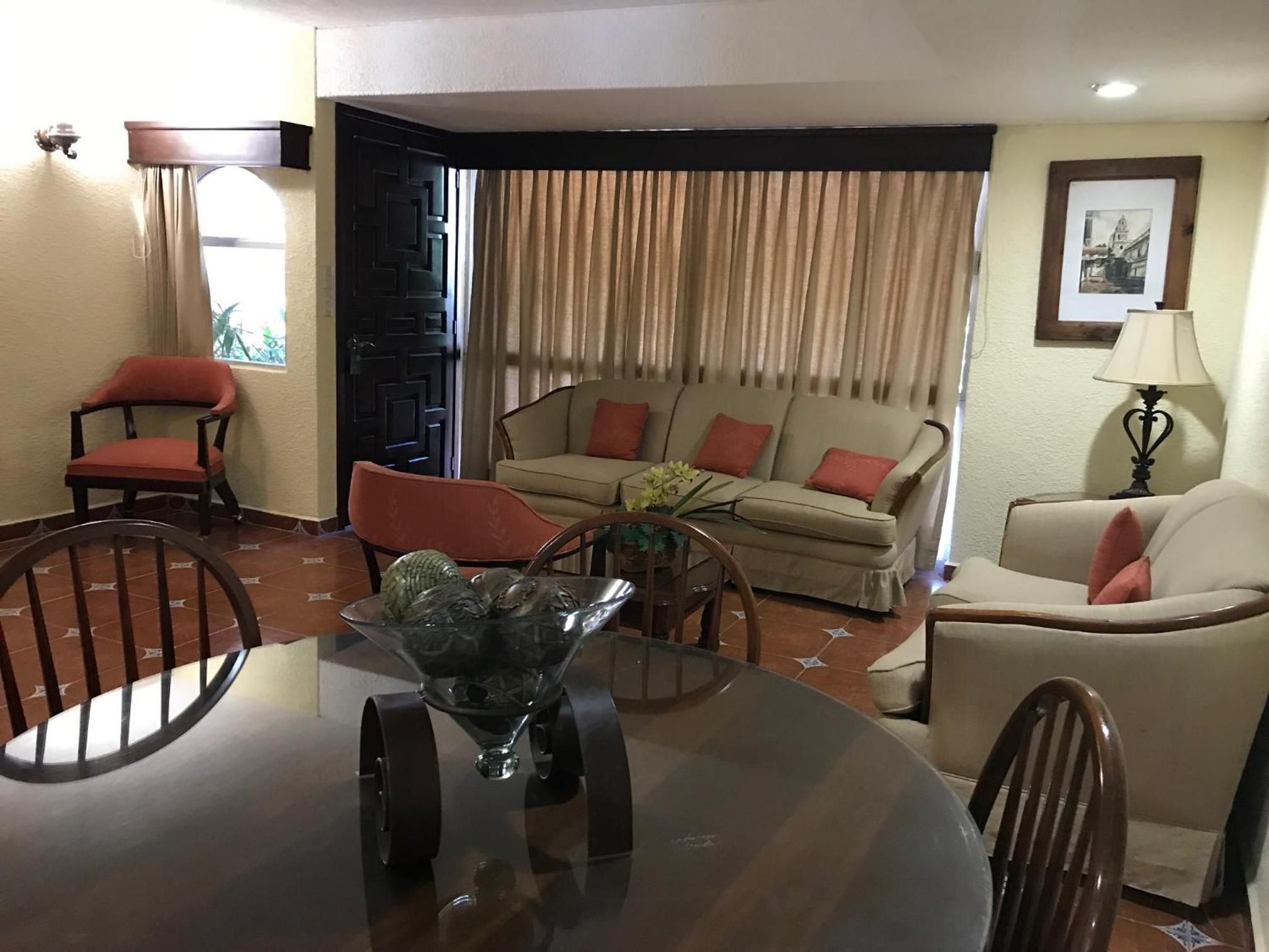 Uma sala de estar com uma mesa de jantar redonda, dois sofás, uma poltrona e um abajur.