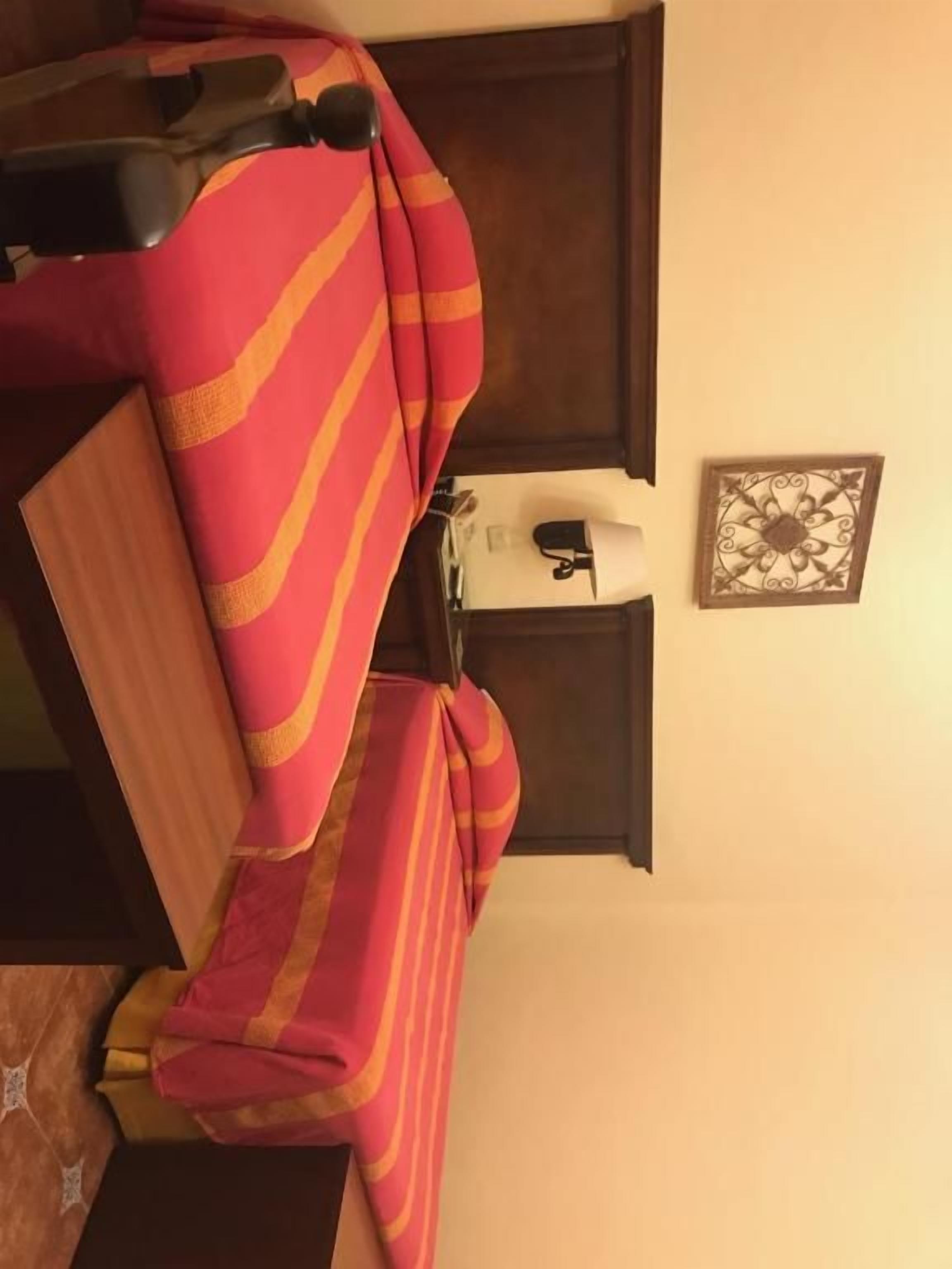 Una habitación con una cama cubierta por un edredón a rayas, una mesita de noche con una lámpara y un adorno en la pared.