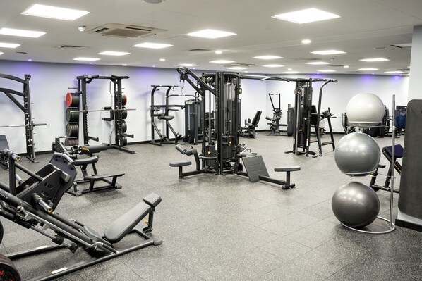 Un gimnasio con diverso equipo de ejercicio, que incluye máquinas de pesas, mancuernas y pelotas de ejercicio.