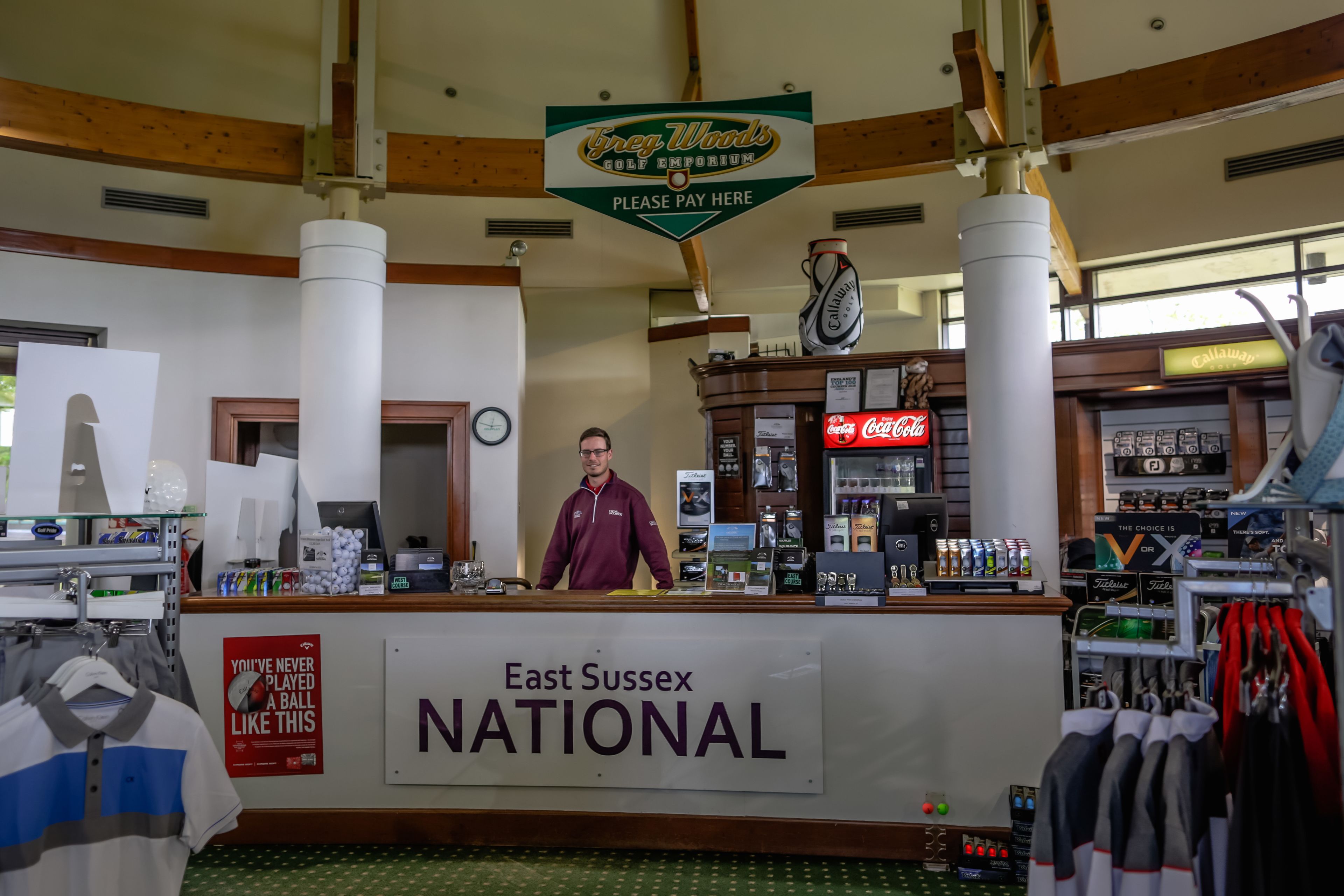 A golf shop interior with a counter, a sign for East Sussex National, and various golf-related items.
