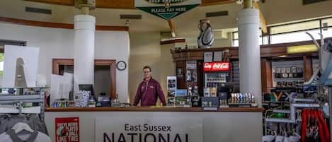 Interior de una tienda de golf, con mostrador, un cartel de East Sussex National y diversos artículos relacionados con el golf.