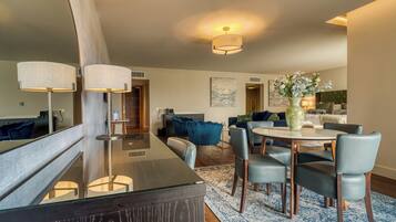 A modern living room with a dining area, featuring a glass-top table, blue and grey chairs, and a large mirror.