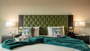 A neatly made bed with a green headboard, two bedside lamps, and floral-patterned pillows.