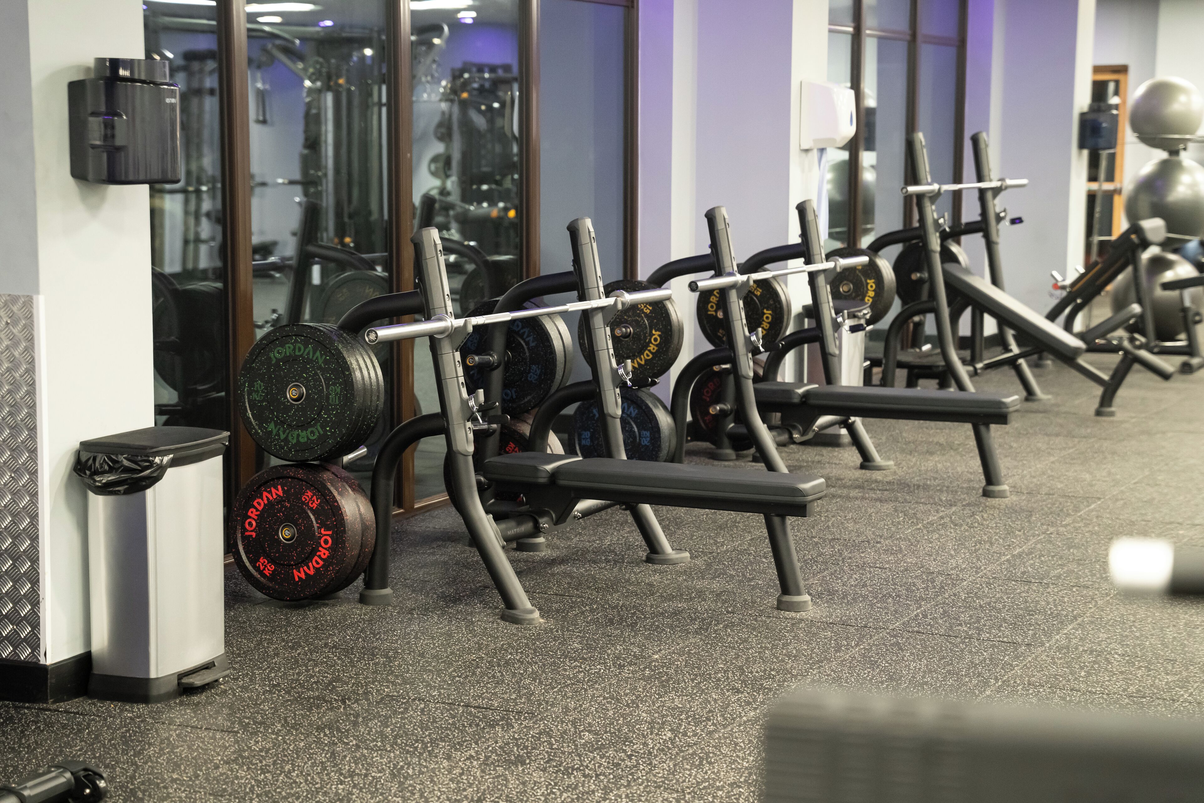 A gym with weightlifting equipment, including barbells and weight plates, and a mirrored wall.