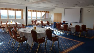 Une salle de conférence dotée de plusieurs tables et chaises, de grandes fenêtres et d’un écran de projection.