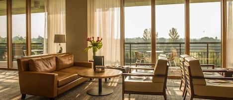 Amplia sala de estar con un sofá de cuero, una mesa redonda de centro y un juego de comedor. Amplias ventanas ofrecen vistas al exterior.