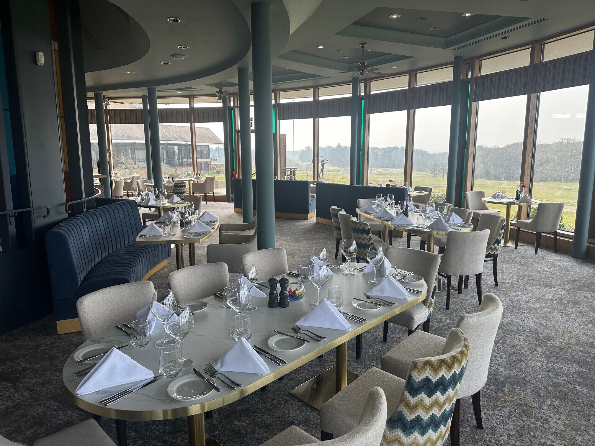 Un restaurante con mesas dispuestas para comer, amplios ventanales que ofrecen vistas al exterior y un ventilador de techo.