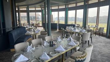 A restaurant with tables set for dining, large windows offering a view of the outdoors, and a ceiling fan.