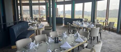 Un restaurante con mesas dispuestas para comer, amplios ventanales que ofrecen vistas al exterior y un ventilador de techo.