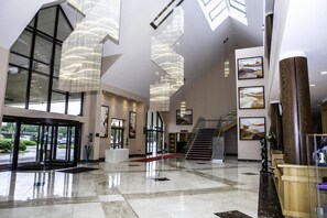 Un vestíbulo amplio con techos altos, ventanas grandes y candelabros modernos.