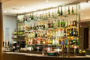 A bar area with multiple shelves of various liquor bottles, a digital clock, and a cash register.