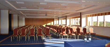 A conference room with rows of chairs, a blue carpet, and large windows.