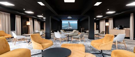 Een moderne hotellobby met een groot scherm waarop een schilderachtig uitzicht te zien is, comfortabele zithoeken en een receptiebalie.