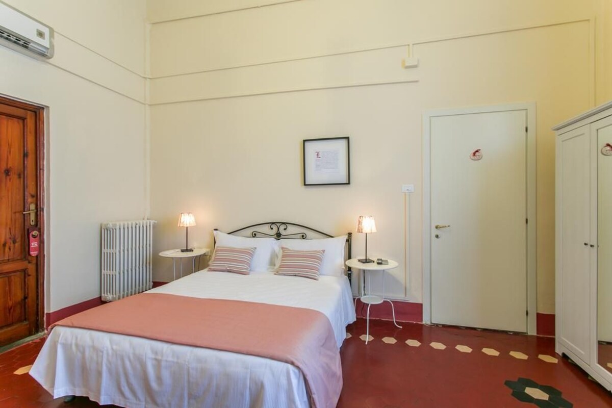 Une chambre d’hôtel avec un lit, des tables de chevet, un radiateur, une porte et une armoire.