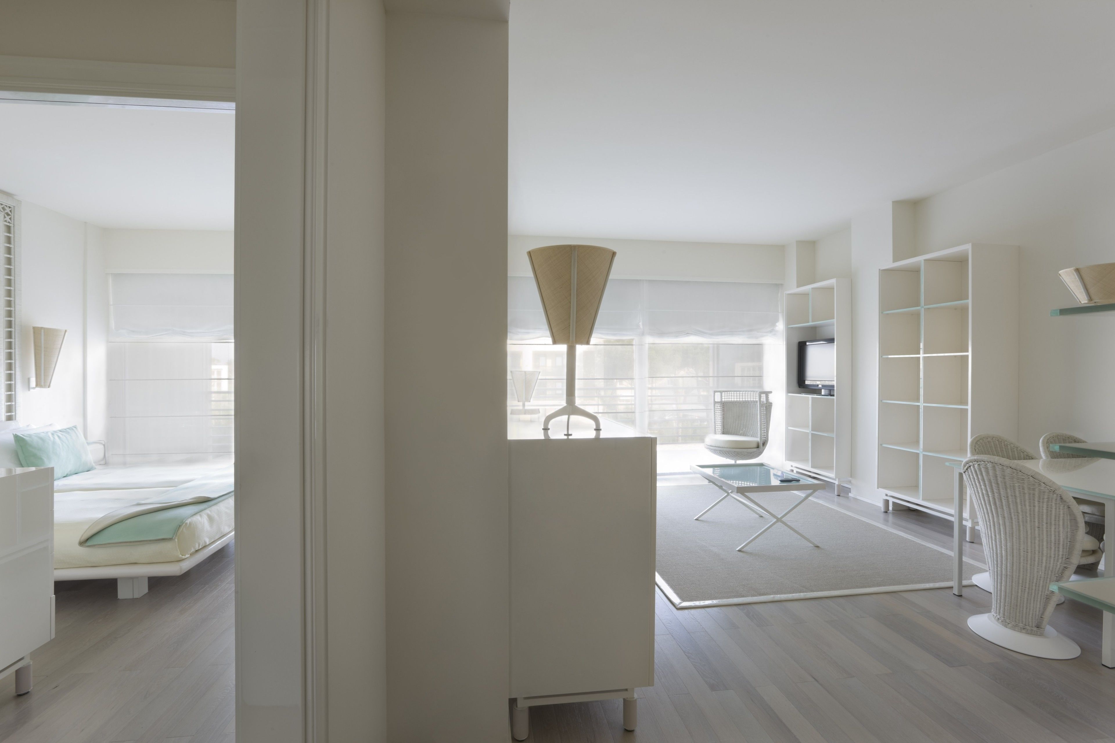 A modern hotel room with a bed, a desk, a chair, a TV, and built-in shelving.