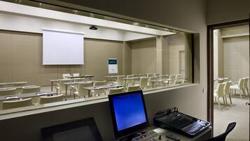 Un salón de conferencias con una pantalla de proyección grande, varias mesas y sillas.