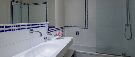 Un baño con un lavamanos blanco, un espejo, cabina de ducha de cristal y un borde de azulejos azules.