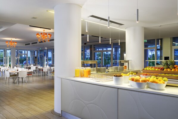 Un espace moderne dédié au petit-déjeuner, avec un buffet, des meubles blancs et de grandes fenêtres.
