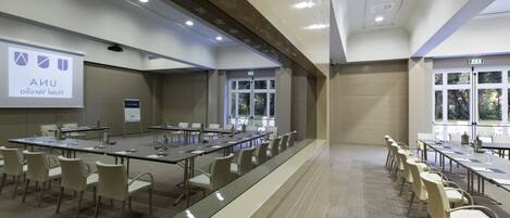 A conference room with long tables and chairs, a projector screen, and a large window.
