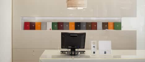 Mostrador de recepción con monitor de pantalla plana, una lámpara y una estantería con libros.