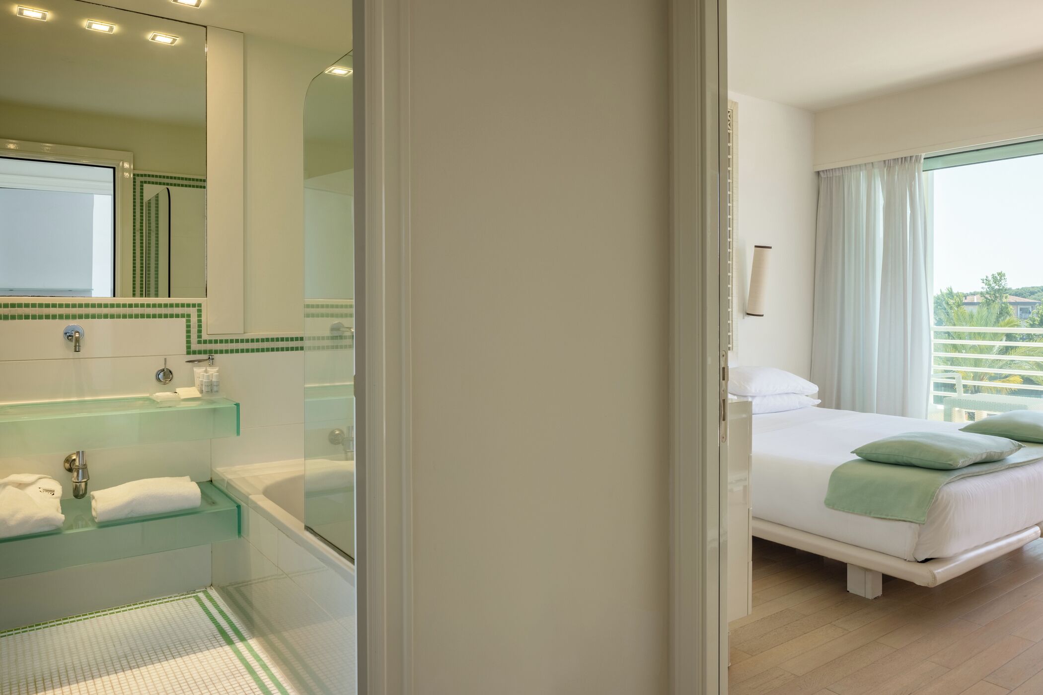 A hotel room with a large bed, a bathroom with a glass shower enclosure, and a view of the outdoors.