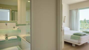 A hotel room with a large bed, a bathroom with a glass shower enclosure, and a view of the outdoors.