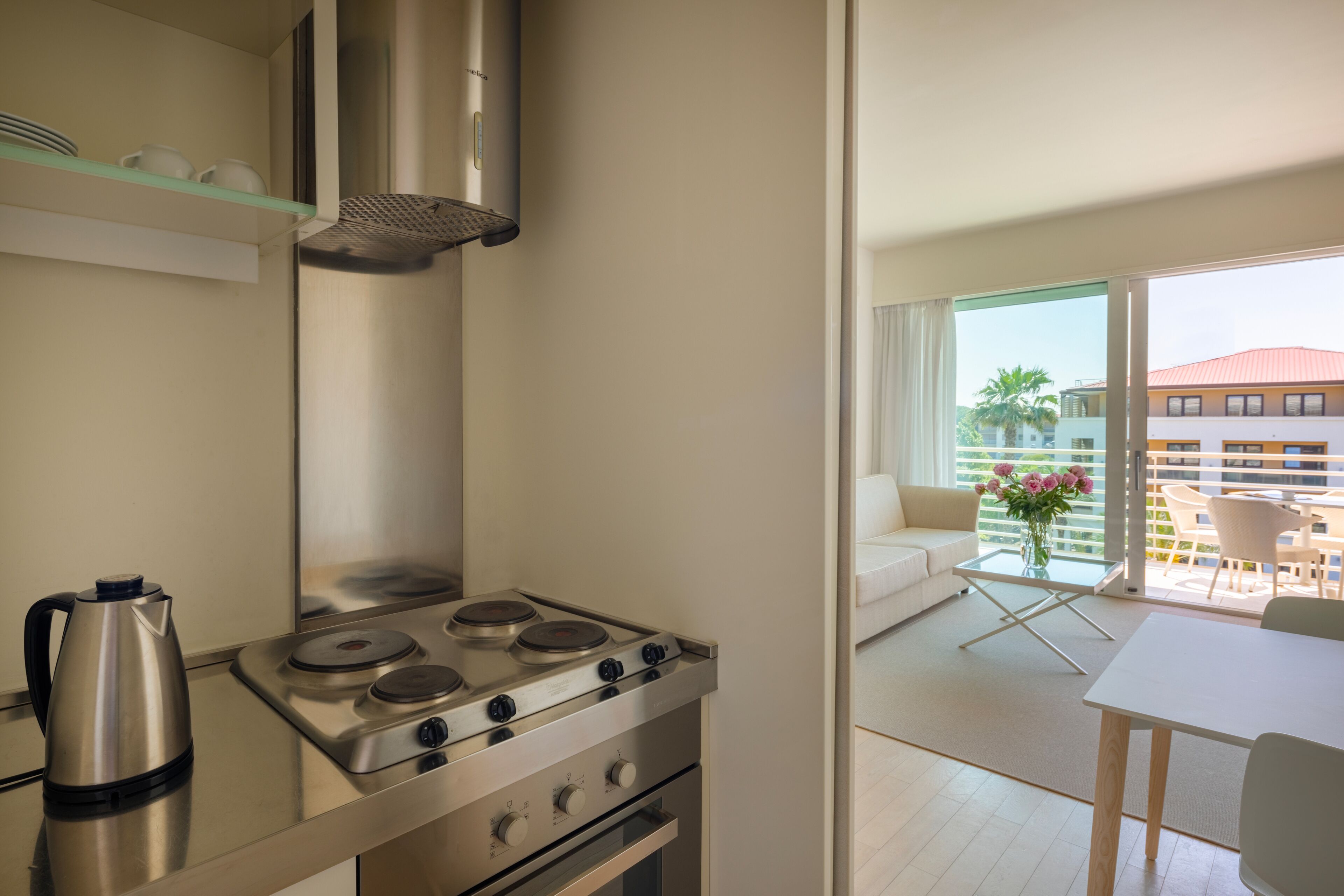 A modern kitchen with a stove, kettle, and glass shelves.