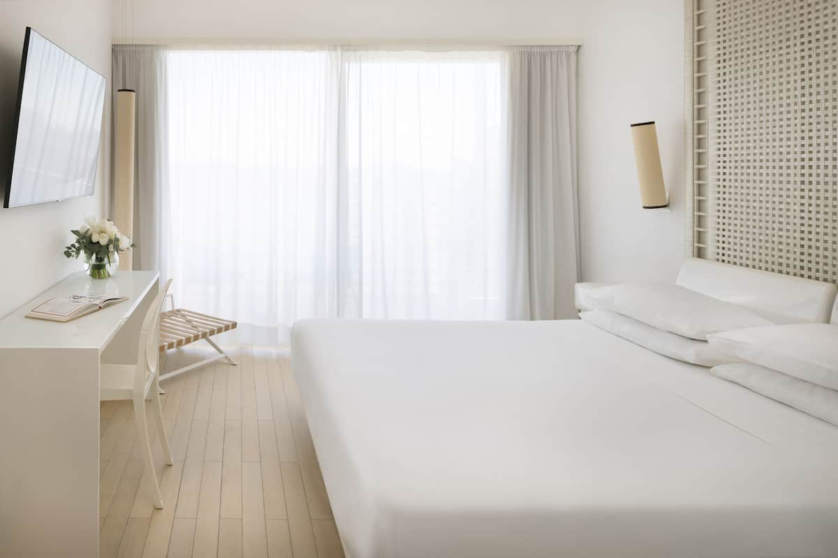 A hotel room with a bed, a desk, a chair, a TV, and a window with curtains.