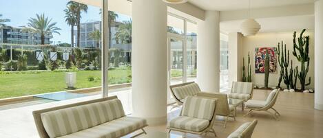 A spacious lounge with wicker furniture, large windows, and a view of a pool and greenery.