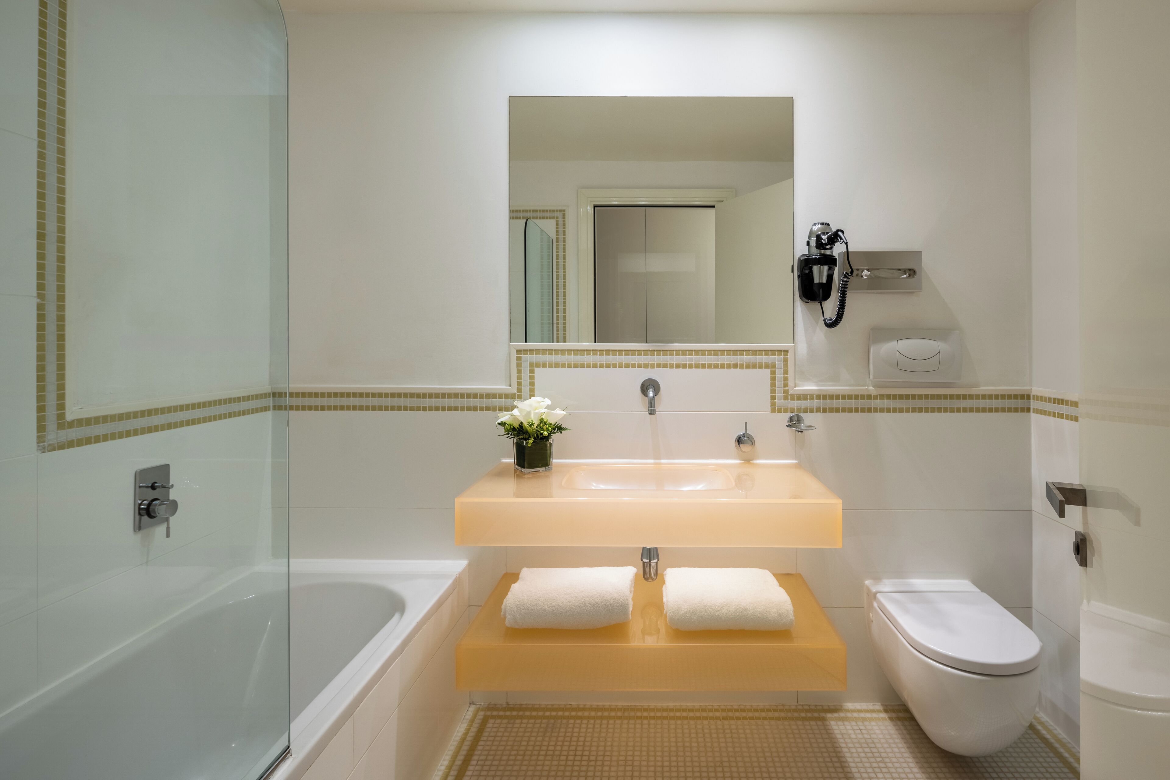 A modern bathroom with a glass-enclosed shower, a white bathtub, a sink with a mirror above, and a toilet.