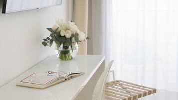 Una habitación moderna y minimalista con un escritorio blanco, un jarrón de flores blancas y un libro.