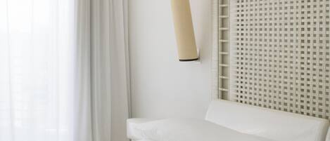 A hotel room with a large bed, a wall-mounted lamp, and a window with curtains.