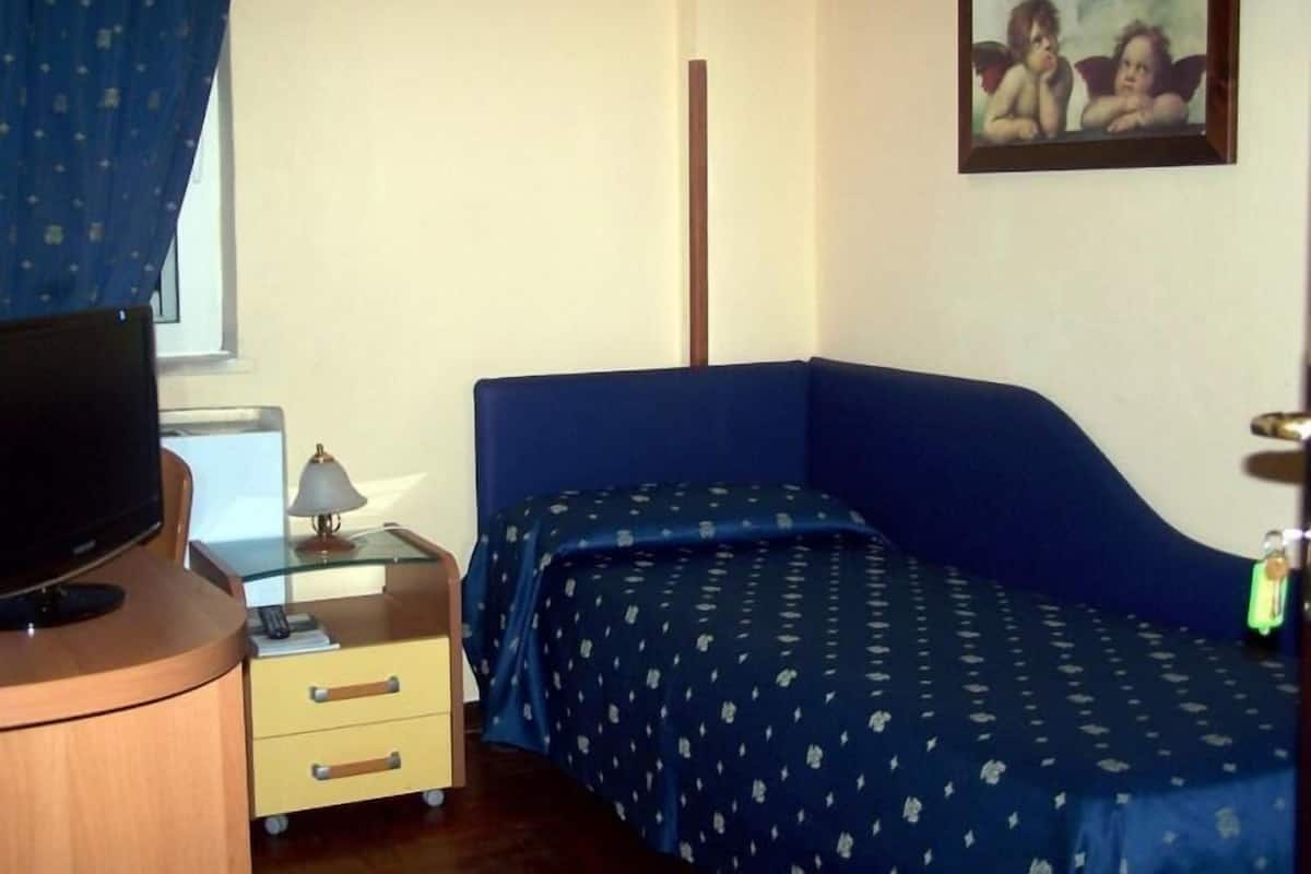 A room with a bed, a desk with a lamp, a television, and a painting on the wall.