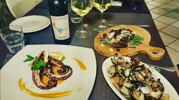 A dining table with plates of octopus and clams, a bottle of wine, and glasses of white wine.