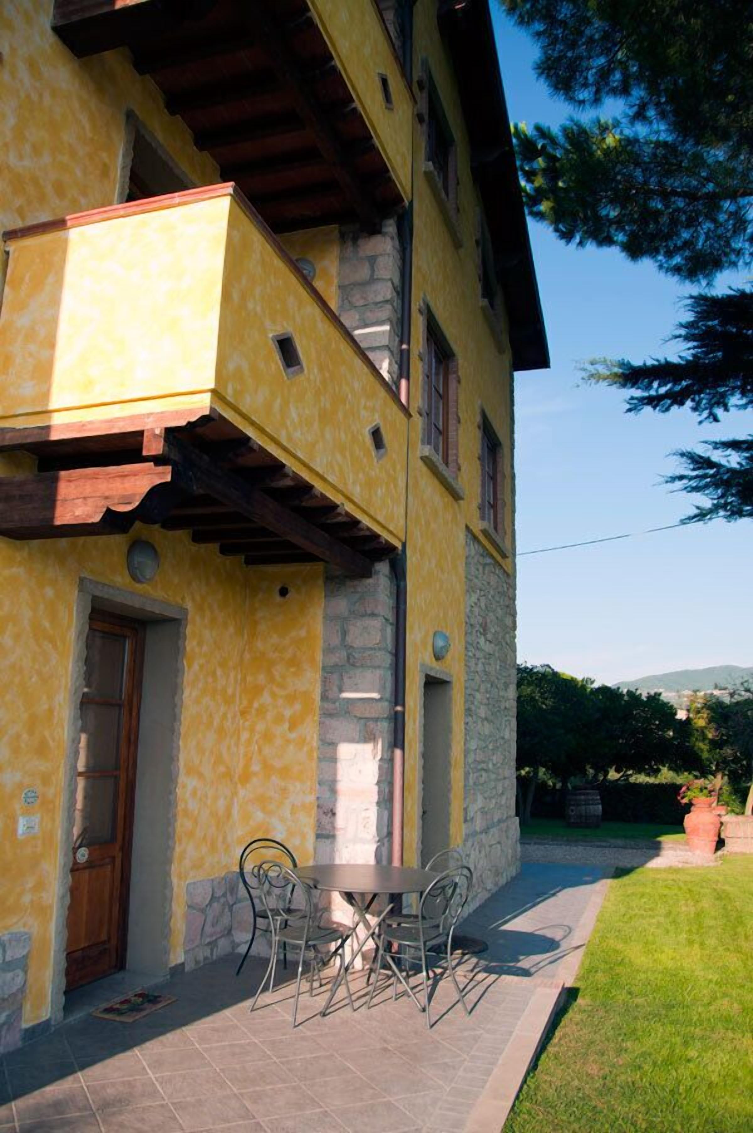 Un edificio amarillo con fachada de piedra, un balcón y un patio con mesa y sillas.