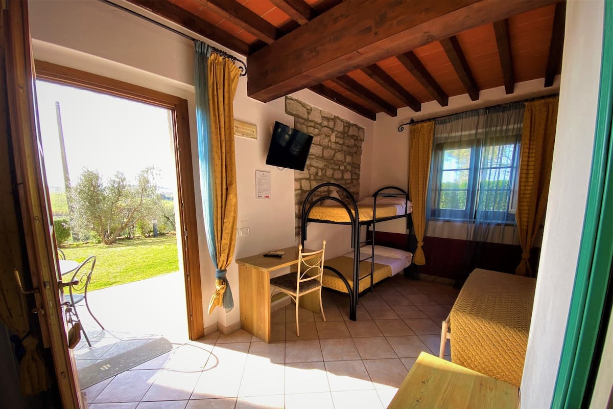 Habitación con literas, un escritorio y una silla. Se aprecia una pared de piedra y un televisor fijado en ella.