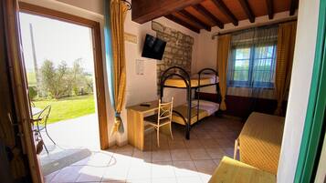 A room with bunk beds, a desk, and a chair. There is a stone wall and a TV mounted on it.